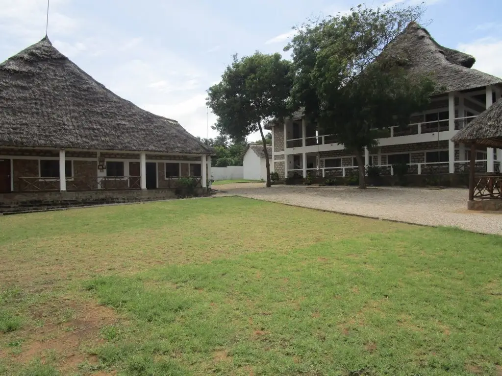 The grounds of the happy house school with a large grass idea and thatched buildings