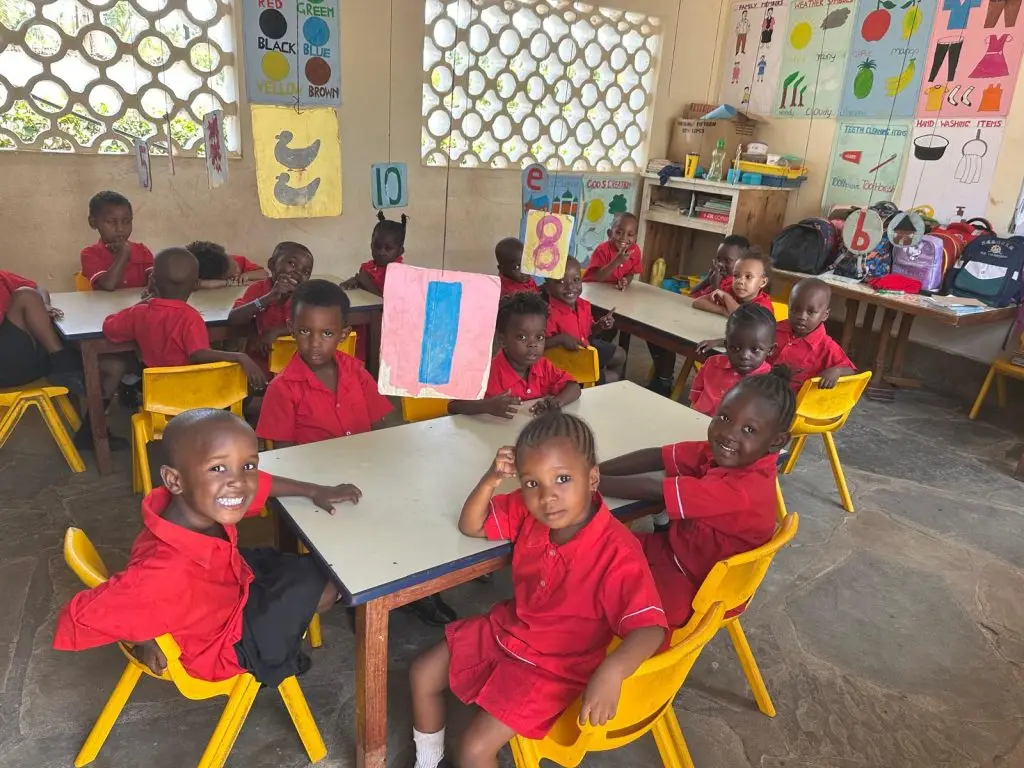 A group of small children at the happy house school wearing their red uniform sat in groups at their table working