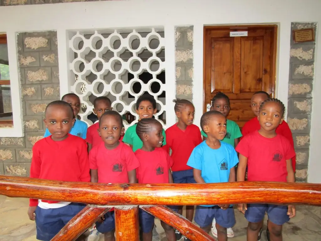 A group of small children in the school uniform with red and blue t-shirts stood smiling